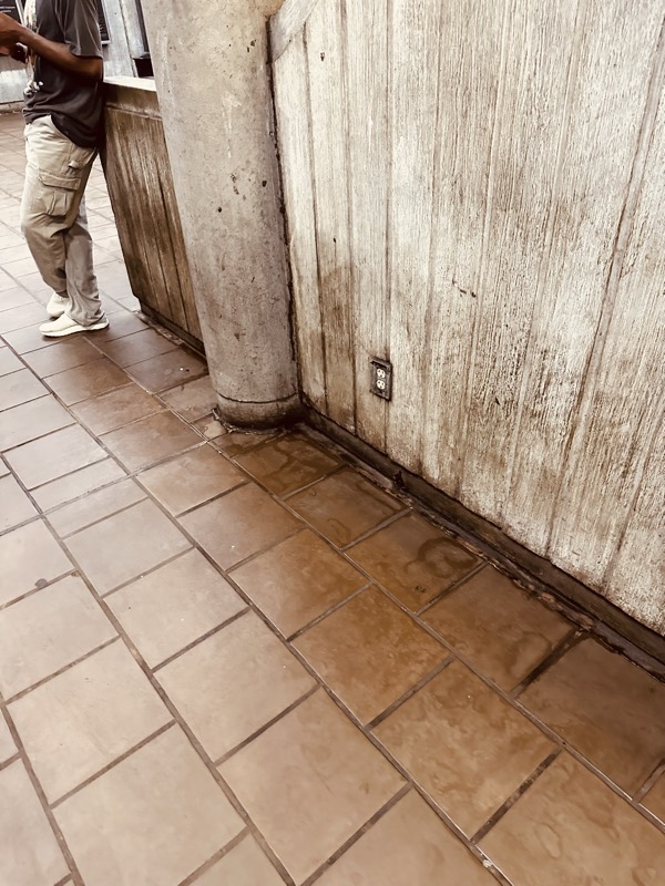 A commuter walks past stained tile flooring next to a weathered board-formed concrete construction barrier in a MARTA station.