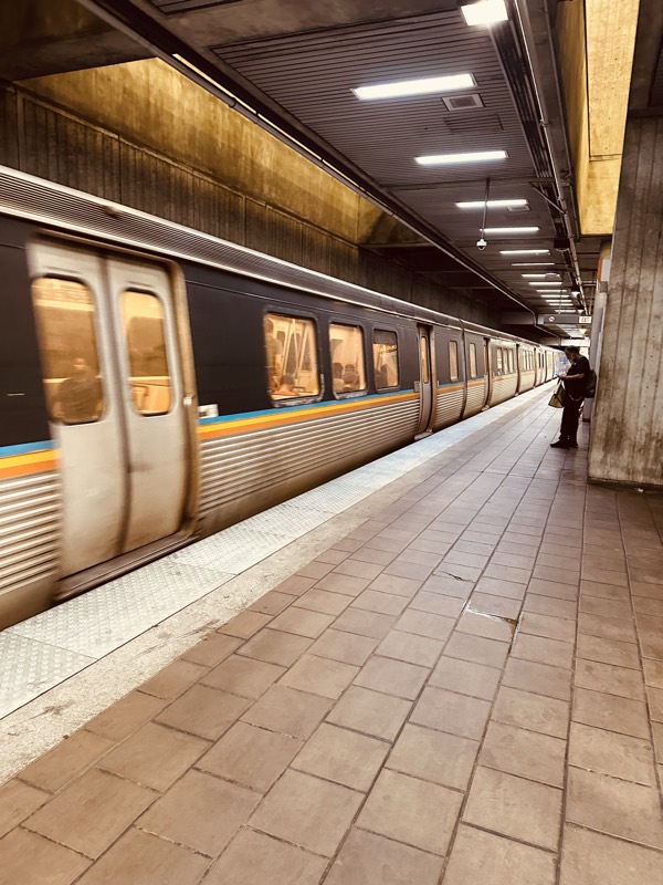 A blurred MARTA train at a station platform, with one commuter waiting on dirty floor tiles.