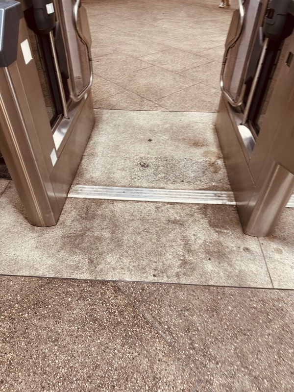 Looking down at the base of a MARTA fare gate, showing heavily stained tile where riders step through.