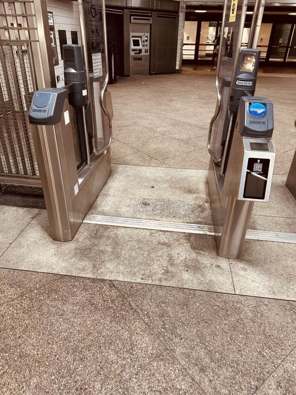 Two fare gates open onto a concourse with a visibly worn tile floor.