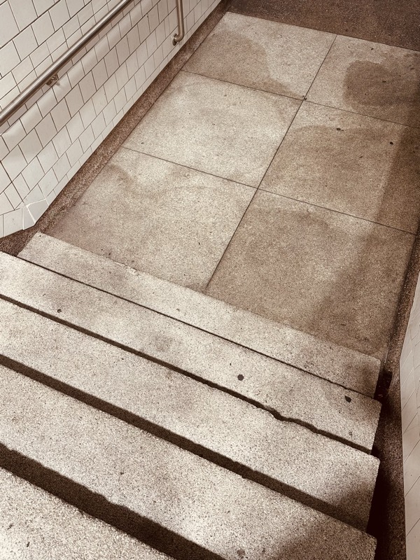 Concrete station stairwell with worn, stained treads and white tile walls darkened over time.