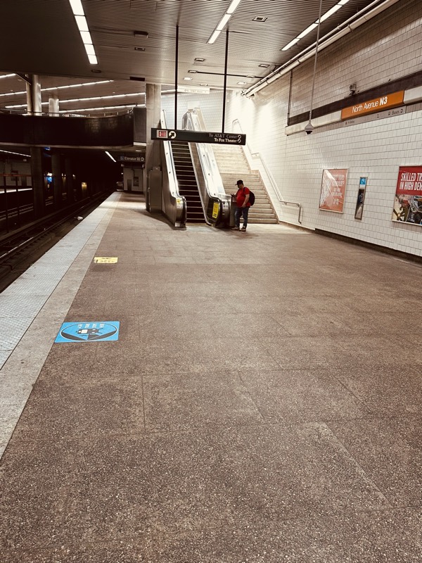 North Avenue station platform showing the escalator and stair entrances, a directional sticker on the floor, and weathered tile underfoot.