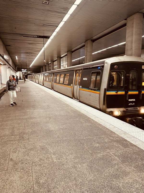 A MARTA train arrives at a station platform with a commuter waiting in the foreground.