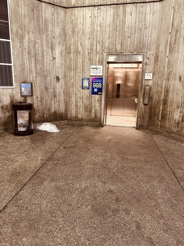 MARTA elevator alcove with weathered board-formed concrete walls and litter on the concrete floor.