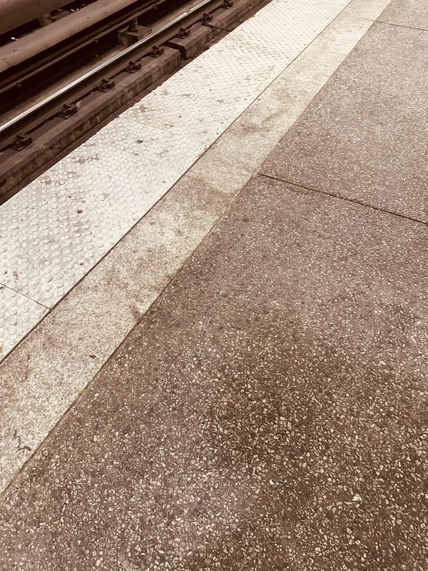 Yellow tactile platform-edge strip alongside a track, with stained concrete platform surface in the foreground.