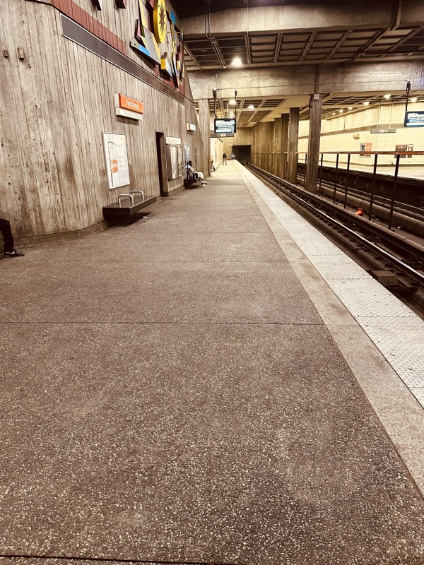 An empty platform in off-peak hours showing a long stained concrete floor and a weathered board-formed concrete feature wall.