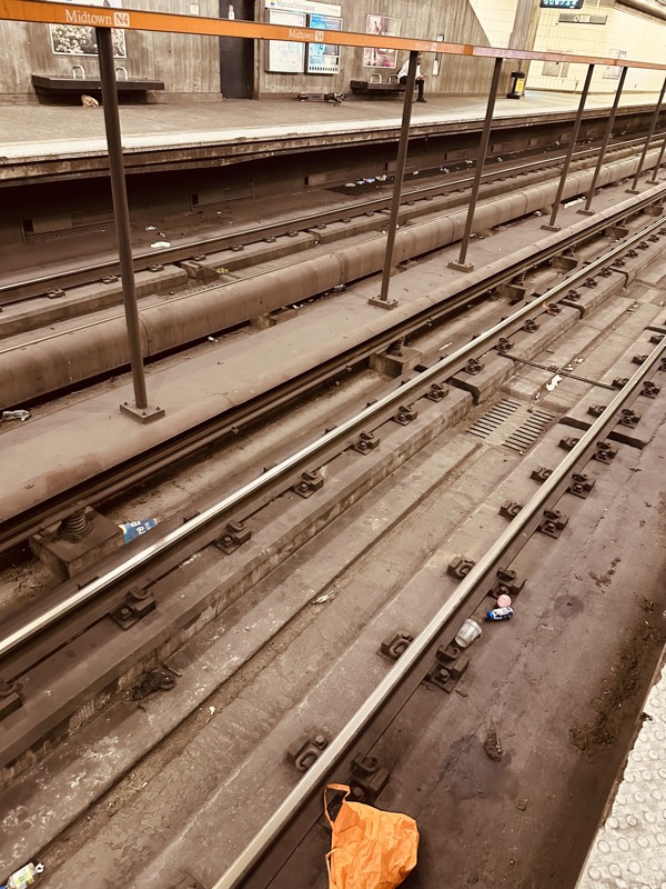 A close view of MARTA track bed showing bottles, fast-food wrappers, and an orange plastic bag among the rails and ties.