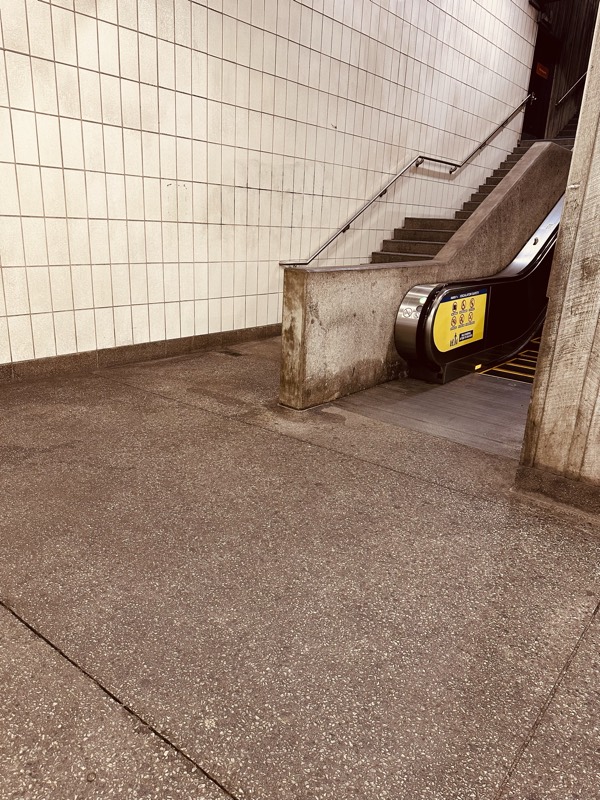 Base of a MARTA station escalator showing a stained, paint-flecked concrete floor.