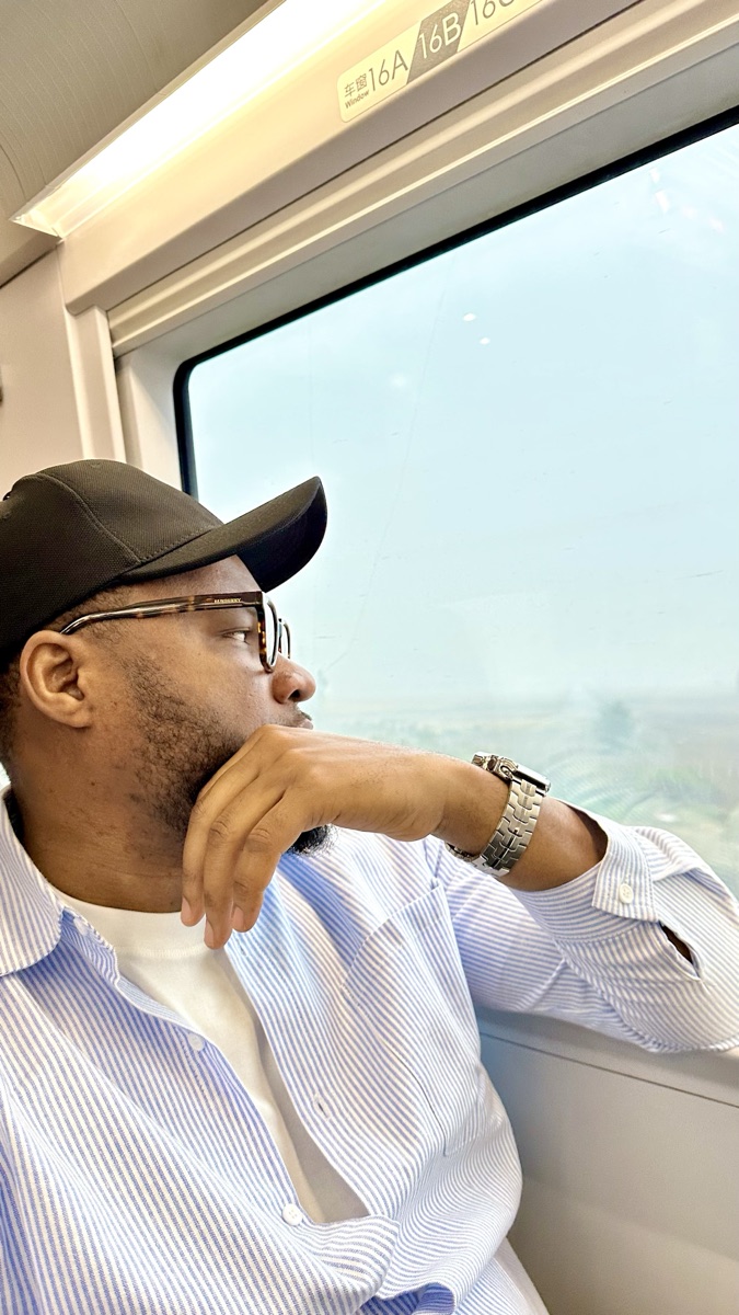 Ernest Timothy looking out the window of a train, considering the city outside.